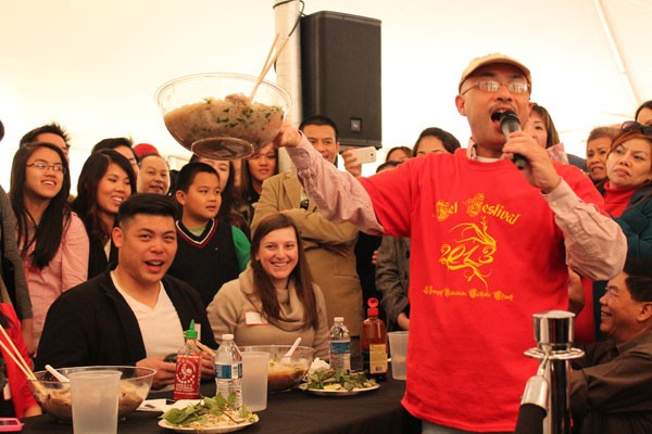 An announcer for the Pho eating competition holds up one of the contestants bowl (Kseniya Martin, pictured sitting at the table on the right) before it is weighed to see just how much she ate.
