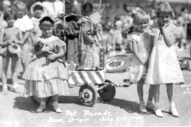 Children with float at Pet Parade, Bend. July 3-4, 1934. The float was a group effort by the children in the neighborhood of Drake Road and Harmon Boulevard. The girl on the left (holding her pet cat) is Genevieve Armstrong. Her sister, Joyce Armstrong, is on the far right (with hand to cheek). Elma Ramlo is to her left (standing slightly behind Joyce). Jackie Lightfoot is standing behind the wagon (holding a hat). She did cartwheels beside the float the entire distance of the parade. - COURTESY  DESCHUTES COUNTY HISTORICAL