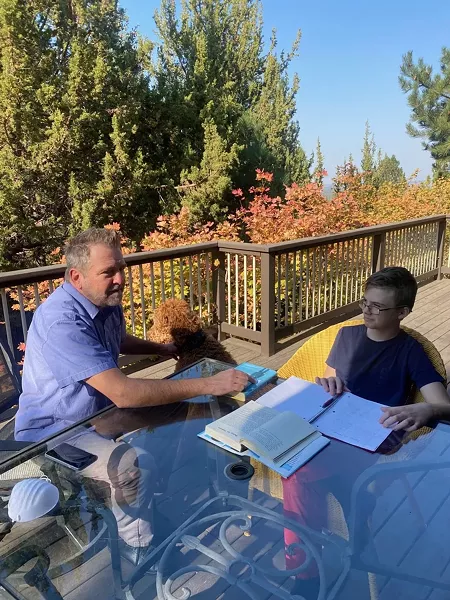 Jason Tierney, the founder of Central Oregon Educational Pods, helps Grayson Graham with distance learning on an outdoor patio. - COURTESY OF JASON TIERNEY