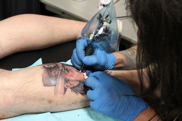 JT, owner and artist for House of Ink Tattoo from Monroe, NC, works on a cowboy piece on Shelby Rummages calf.