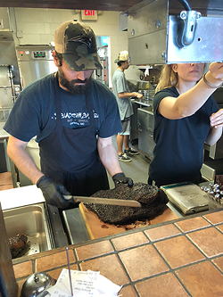 An employee begins to slice off pieces from a brisket. (Photo by Sophie Whisnant)