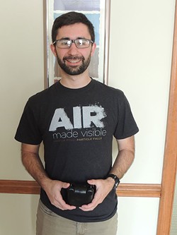 Calvin Cupini holds an AirBeam, used to measure air quality at different points around the city. - RYAN PITKIN