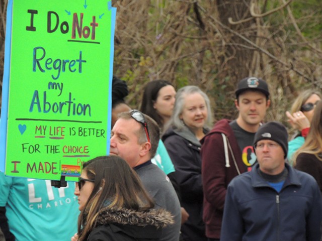 A pro-choice counter-protester stands between a large group of prayer marchers and A Preferred Women’s Health Center in east Charlotte.