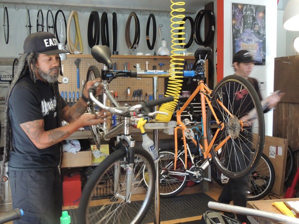 Dread (left) and Cory work on bikes at The Spoke Easy. The orange bike had been hit by a car the previous day. (Photo by Ryan Pitkin)