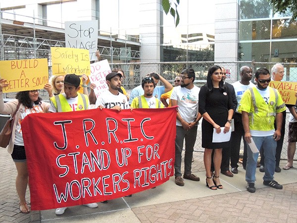 Supporters of the Justice and Respect in the Reinforcing Industry Coalition stand outside the Charlotte-Mecklenburg Government Center. To the right, in yellow, Alexis Gonzalez prepares to address media. (Photo by Ryan Pitkin)