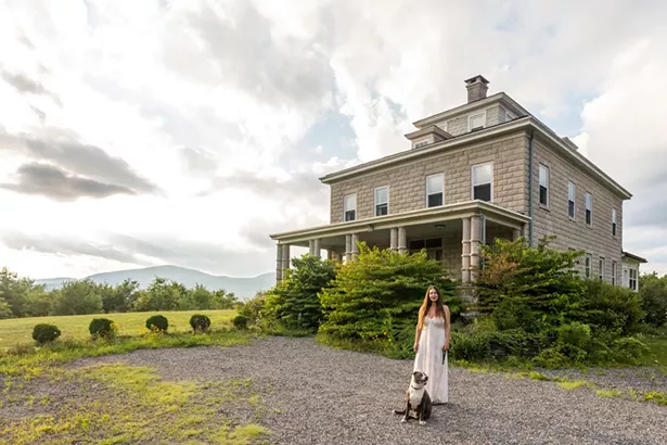 Diane Raimondo and her dog Layla in front of her hundred-year old stone house. Overlooking the Ashokan Reservoir, the historic home was built by the Ashokan’s chief engineer, J. Waldo Smith. - PHOTO BY WINONA BARTON-BALLENTINE