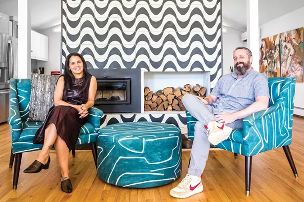 Ana Claudia Schultz and Aaron Smyle in - their open-concept living room. By removing stone - wing walls from the fireplace, they opened the - space to the adjacent kitchen and dining area. The - blue-and-white chairs are made of fabric designed - by Kelly Wearstler—Schultz sourced the same - fabric and then commissioned a matching ottoman - from her upholsterer. The abstract painting in the - dining room is by Ryan Wheelbarrow. - PHOTO BY WINONA BARTON-BALLENTINE