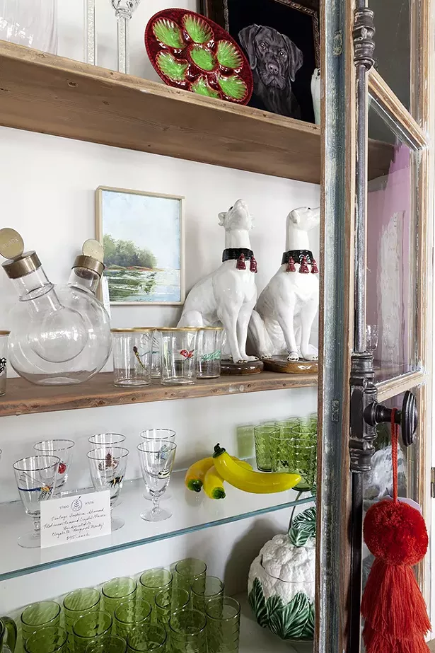 The glass cabinet showcases painted glassware by Elizabeth Hargraves Mandy, a local artist based in Millbrook who focuses on restoration work. The dogs are in the style of Victorian continental greyhound statues which are from the late 1800s. The pieces are indicative of the sort of pieces sourced by the studio: cheeky vintage sculptures, glass bananas, and delicate glass carafes from Paris fleas.