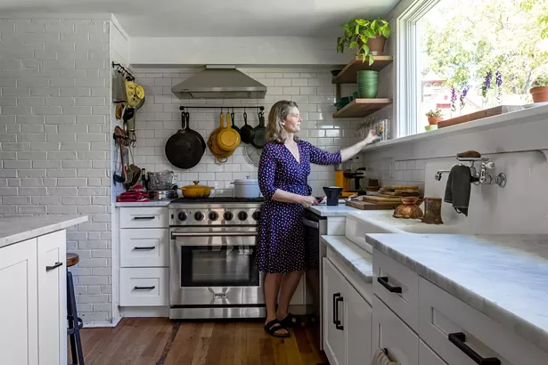 Kathy Reisfeld in the home’s new kitchen, which had been badly damaged by flooding before the couple bought the home. With the help of architect Inma Donaire, they reimagined the space to include a modern rectangular window capturing the arboreal view. “The home feels like it has its own life to it,” explains Reisfeld. “It feels like we are just custodians of this place for a while.” - WINONA BARTON-BALLENTINE