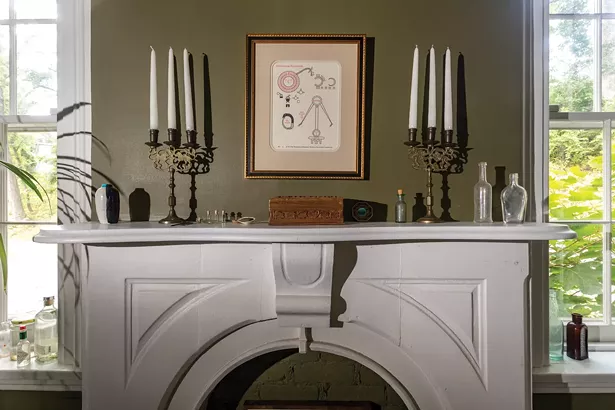 A fireplace mantel in Jesse Bransford’s study is one of several altars in the octagonal Catskill house. An alchemical print from Ouroboros Press sits above candlesticks and found objects.