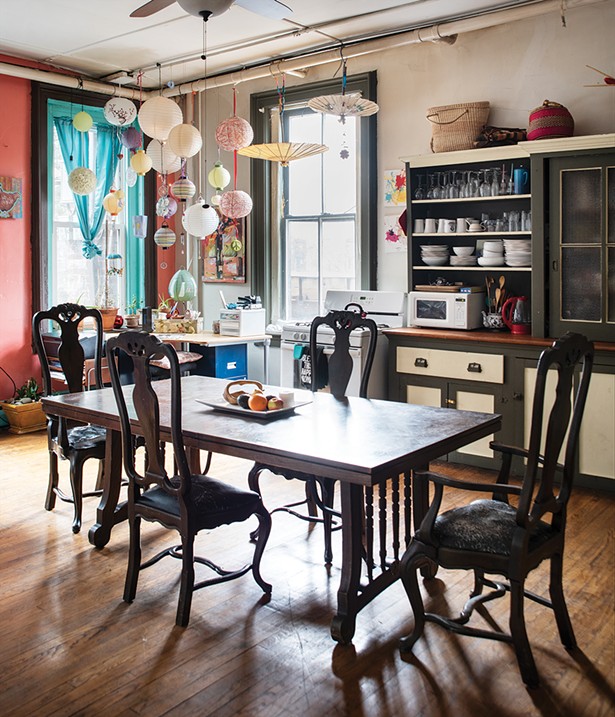 The loft’s main kitchen looks over the backyards over the neighboring buildings. Bickman painted the wall and trim a contrasting orange and blue, but left the original sideboard grey and yellow. Over the desk, she camouflaged some unsightly pipes with hanging lanterns and mementos. - PHOTO BY DEBORAH DEGRAFFENREID