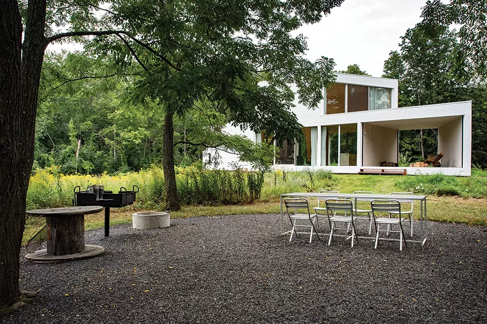 Looking back at the house from the outdoor kitchen and dining area. With multiple doors throughout the house allowing access between the landscape and the home’s interior, the couple and their guests use the - home and campsite features interchangeably during the warmer months. “There’s an interplay of elements within the wrapper of the house,” explains Leven, “but also within the wrapper of the landscape and sky, and - even within the wrapper of the Hudson Valley.” - PHOTO: DEBORAH DEGRAFFENREID