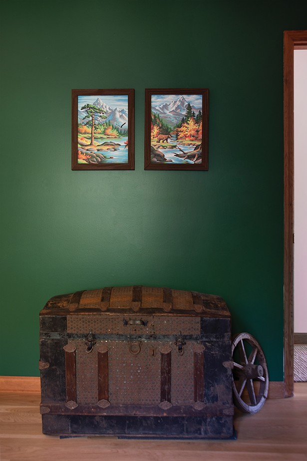 The couple painted an accent wall in the first-floor guest room to add a pop of green. Originally they’d thought to decorate the home with a “rustic-modern vibe” and collected trunks, weathered crates, and paintings from upstate flea markets. After deciding on a different aesthetic for a majority of the house, they conceded to decorate the guest room with their upstate finds, including an antique trunk, oil paintings, and a collection of maps. - PHOTO: DEBORAH DEGRAFFENREID