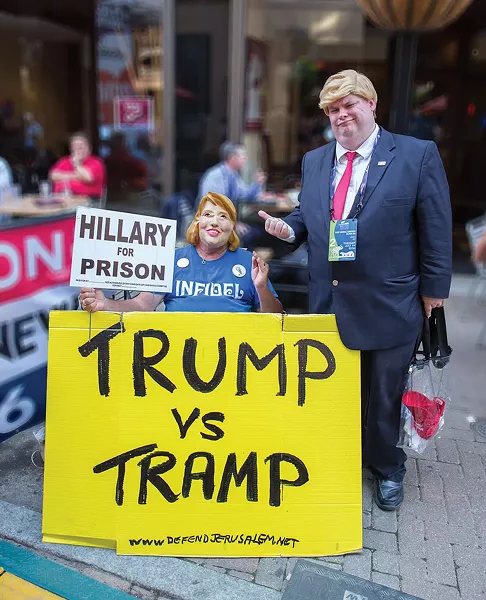 Political dramatist acted out their slogans on East 4th Street. The reference at the bottom of the yellow placard refers to an organization that memorializes Holocaust sites. - FRANK SPINELLI