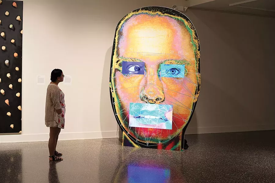 Ashley Galarza, gallery assistant, in front of #ISO, a 2015 work made from wood, inkjet print, LCD screens, and USB flash drives by Tony Oursler, with sound by Josie Keefe and Laura Hunt, at the Samuel Dorsky Museum of Art. - JOHN GARAY