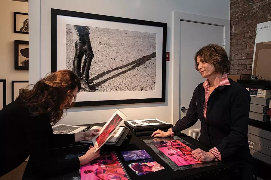 In Rice’s studio, she and neighbor Amy Pilkington look over Rice’s pictures of Studio 54’s opening night. A fellow artist, Pilkington also modeled for the print hanging along the back wall entitled “Woman in Chaps” Bridgehampton, NY. - PHOTO: DEBORAH DEGRAFFENREID