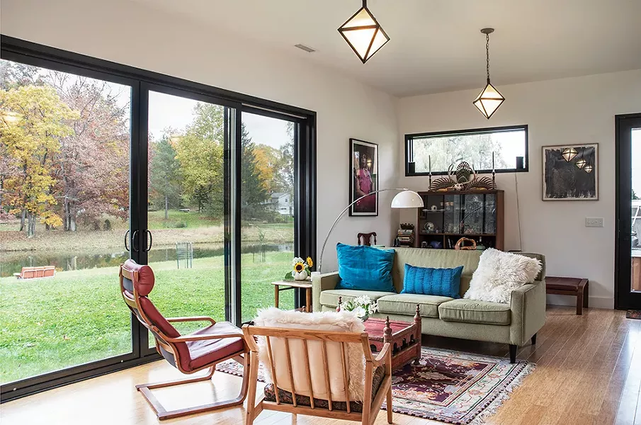 The home’s living room faces east over the pond. Lady Marmalade by local artist Nadine Robbins hangs along the eastern wall; the painted skull on display at top of the bookshelf was painted by Schmidt’s mother. The hanging lamps are from Nectar, formerly in Rhinebeck. - PHOTO: DEBORAH DEGRAFFENREID