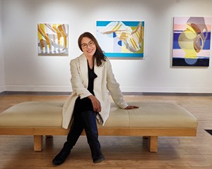 Carrie Chen in front of paintings by Ginnie Gardiner in the Carrie Chen Gallery.
