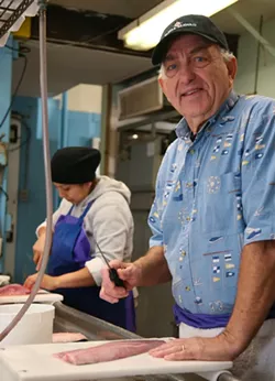 Charlie Russo, Jr. bones up on his knife skills with a local shad, along with employee Blanca Perez. - PHOTO BY JON WAITS