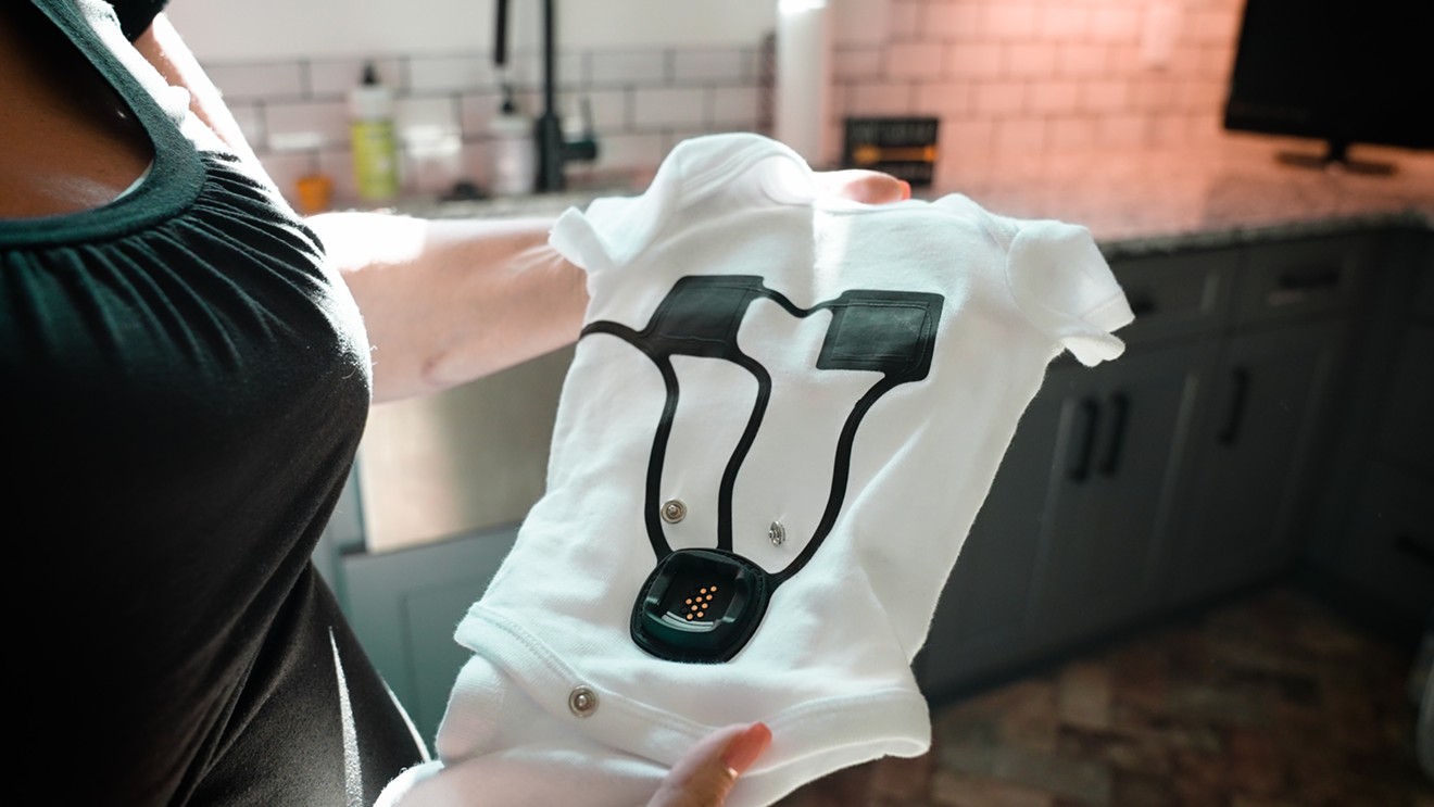 Hands hold the Sensoria Baby onesie, equipped with sensors that can track an infant’s sleep time and breathing rate.