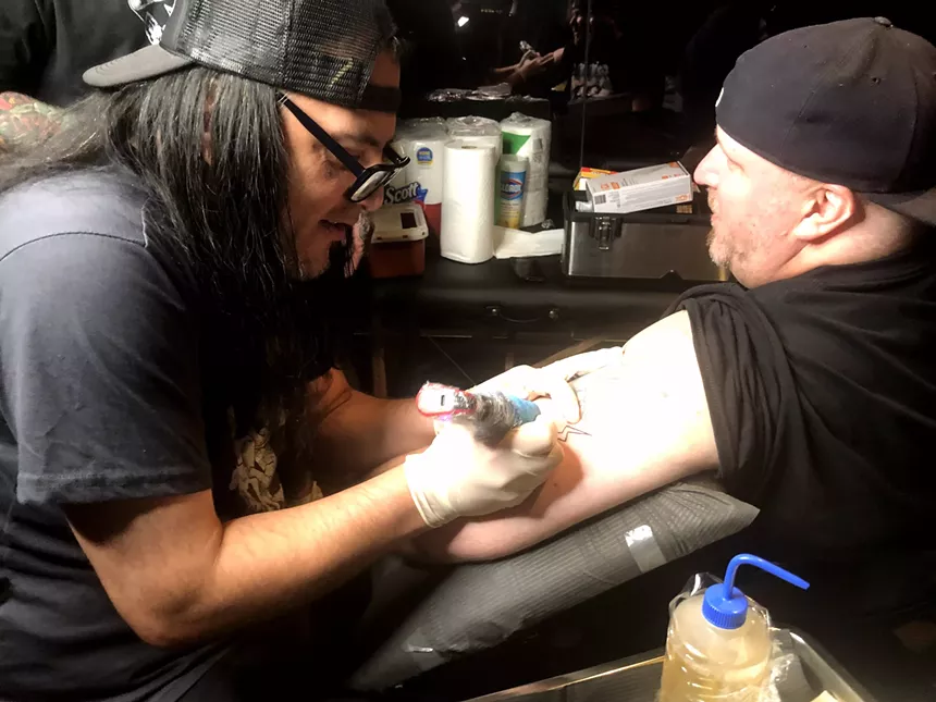Amplified consultant Scott Long, right, gets a tattoo of the Amplified logo on his arm from Cedar Springs Tattoo artist and Dallas musician Bob Zilla. - DANNY GALLAGHER