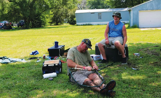 Carl Peiffer mends a broken net the traditional redneck way, with duct tape and nylon cord, while son Tim Peiffer looks on. - PHOTO BY BRUCE RUSHTON