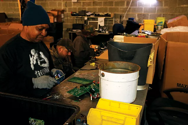 WL Tillman (front) and Ethan Rainey (back) break down circutboards at the deman station (recycle station) in BLH’s warehouse connected in the back. Boxes filled with circuit boards flood the processing area of BLH, where employees remove parts that - PHOTO BY BRANDON TURLEY