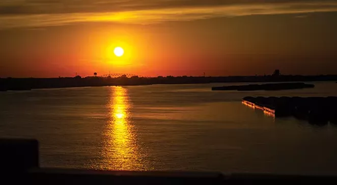 The sun sets over the Ohio River, looking back towards Cairo on the left. Barges sit parked in the water, waiting for river levels to go down far enough for boats to ferry them north. - PHOTO BY MADELYN BECK