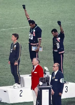 American sprinters Tommie Smith and John Carlos, along with Australian Peter Norman, during the award ceremony of the 200 - meter race at the Mexican Olympic games. During the awards ceremony, Smith (center) and Carlos protested against racial discrimination. They went barefoot on the podium and listened to their anthem bowing their heads and raising a fist with a black glove. Mexico City, Mexico, 1968. - PHOTO BY ANGELO COZZI