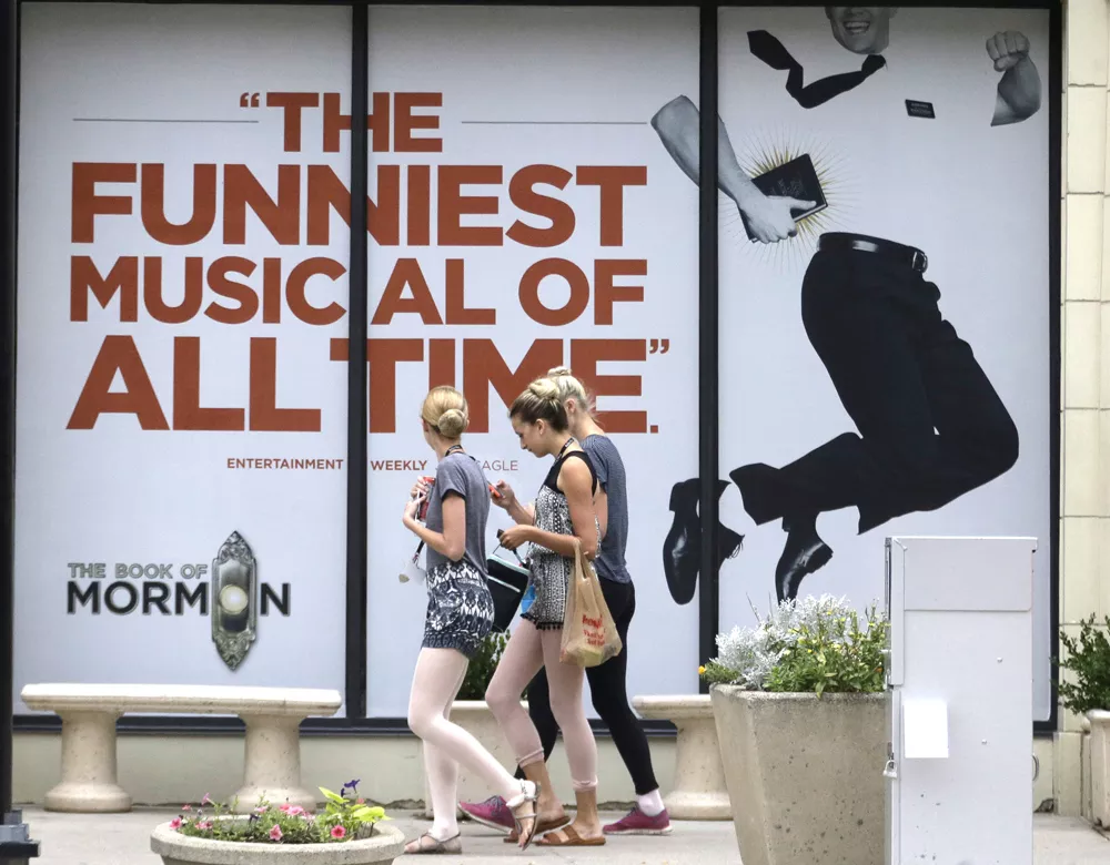 People walk past signs announcing the "Book of Mormon" musical at the Capitol Theatre, Monday, July 27, 2015, in Salt Lake City. The biting satirical musical that mocks Mormons is finally coming to the heart of Mormonlandia, starting a sold-out, two week run on Tuesday, July 28, 2015, at a theater two blocks from the church?s flagship temple and headquarters. - AP PHOTO/RICK BOWMER