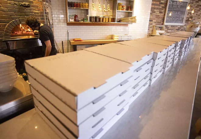 Ivan Saueracker puts a log on the fire in the pizza oven at Maialina on Thursday in Moscow. Pizza boxes for take-out orders are stacked on the counter. - AP