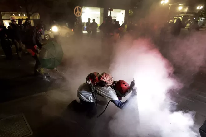 A demonstrator kneels and uses a makeshift shield as federal agents launch tear gas during a Black Lives Matter protest at the Mark O. Hatfield United States Courthouse Wednesday, July 29, 2020, in Portland, Ore. - AP PHOTO/MARCIO JOSE SANCHEZ