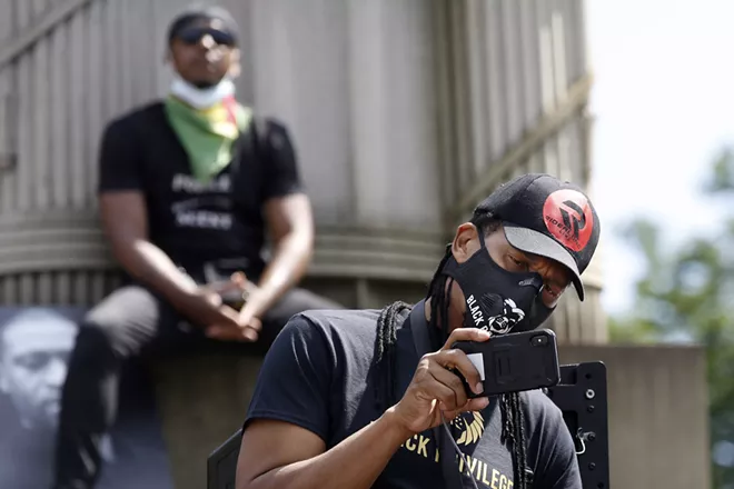 A man uses his cell phone to record speakers as another listens from the pedestal of a column during a Caribbean-led Black Lives Matter rally at Brooklyn's Grand Army Plaza, Sunday, June 14, 2020, in New York. - AP PHOTO/KATHY WILLENS