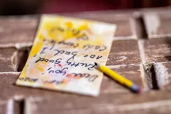 A paper and pencil with the words "Dear you, pretty good, not bad, I can't complain" is written sits on a desk in one of Rachel Jameton's miniature pieces.