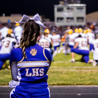 Lewiston High School cheerleader Natalie Wilson takes a knee for an injured player during the annual Lewiston/Clarkston football game at Adams Field. Photographed by Max Moore.
