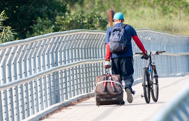 A gentleman drags a bicycle and rolling suitcase with lopping shears strapped to the back over Sandifur Bridge on the morning of Friday, June 29. - DANIEL WALTERS PHOTO