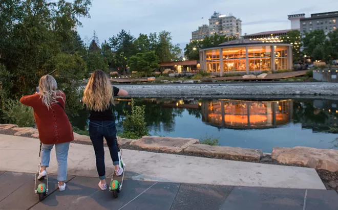 Two Lime scooter riders look across the Spokane River to the Looff Carrousel in Riverfront Park. - DANIEL WALTERS PHOTO