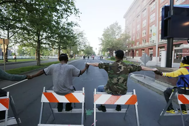 Demonstrators sit on barricades they set up on W. Spokane Falls Blvd., in front of Riverfront Park. - YOUNG KWAK