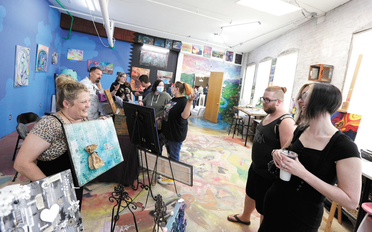 Artist Melanie Campbell shows a mixed media piece to Crystal Lebsock and Leon Phox during M.A.D. Co. Lab Studios' vendor market. - YOUNG KWAK PHOTO