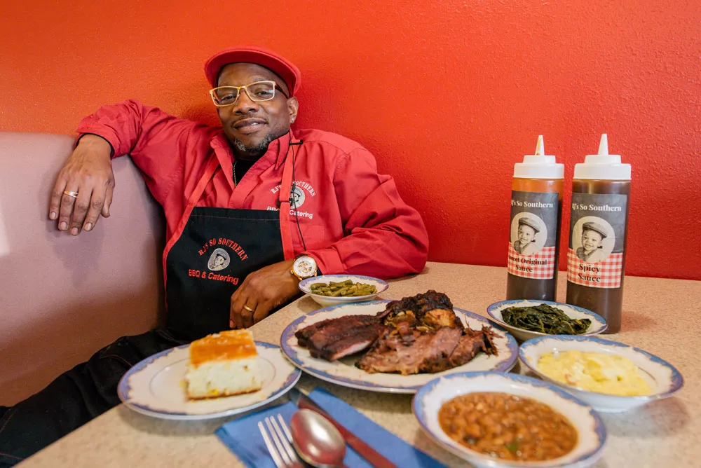 Reggie Perkins sits with some of his Nashville-inspired cuisine at his North Spokane barbecue spot. - ERICK DOXEY