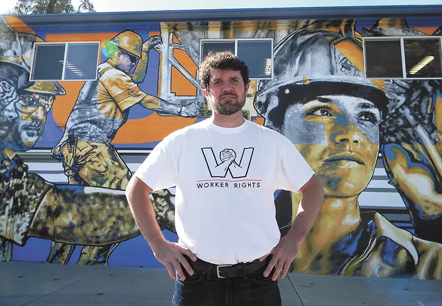 Kai Huschke, the campaign coordinator for Envision Worker Rights, stands next to a labor-themed mural. - JAKE THOMAS