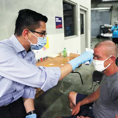 Mohammad Keshtkar, left, a volunteer with the Spokane Regional Health District, checks Rob Mesler's temperature while conducting a COVID-19 screening in July.