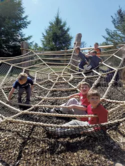 Children climbing on a spider web play structure in VINS' Adventure Playscape - COURTESY OF VINS