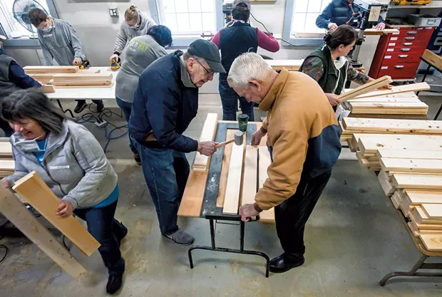 Volunteers use a mallet to make holes in wood that will eventually become a bed - GLENN RUSSELL