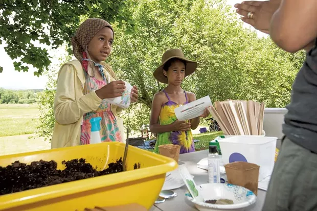 Ava Mirembé and Esmé Ssanyu Grundy Bruce listen to Hanron's instructions at the black eyed peas and collard greens planting station at the Juneteenth celebration - CAT CUTILLO