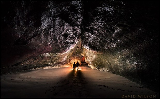 Inside the cave from the deep interior. it may look low at the camera’s end, but it was tall enough for me to stand next to my tripod. That’s my brother and me down there, our shadows complementing the ceiling’s great cleft. Camel Rock is lit up red outside the entrance, illuminated by the headlights of a car up on the cliff behind us. - COURTESY OF DAVID WILSON