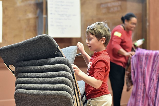 Six-year-old Miles Edrington, who has attended the planing meetings with his mother Allison Edrington, helps put chairs away. - PHOTO BY MEGAN BENDER