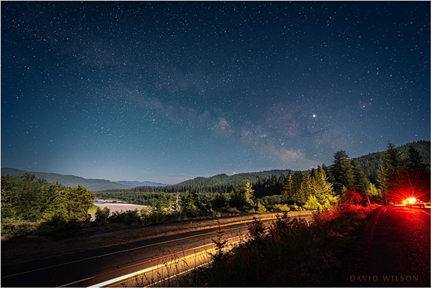 A nighttime view over US Highway 101 and the Eel River valley beneath the Milky Way as seen from a Vista Point in Humboldt County, California. A waxing half moon brightened the sky and cast its illumination on the landscape. The parked car of another night watcher added an unexpected red glow when it turned on its lights. - DAVID WILSON