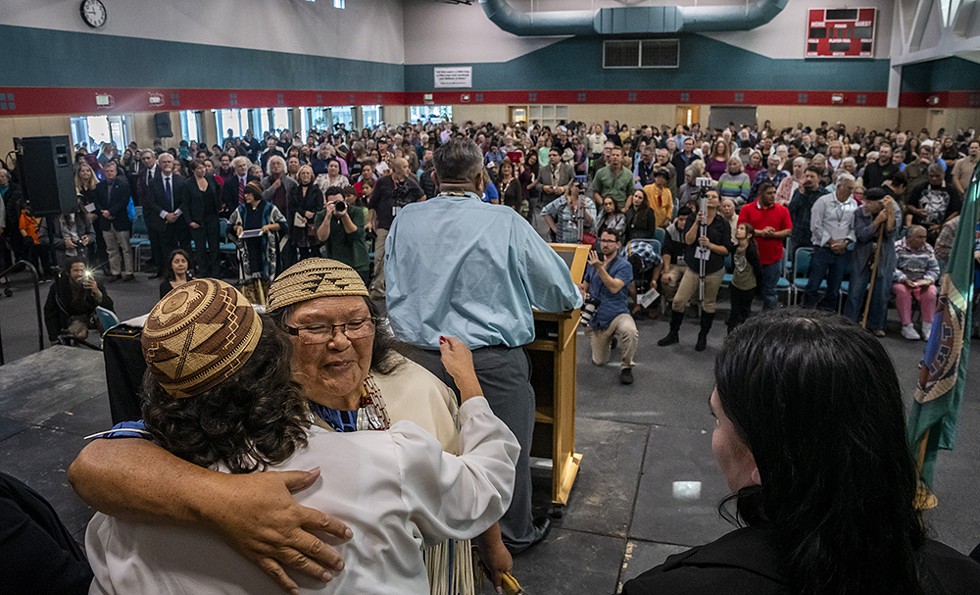 As Wiyot Tribal Chair Ted Hernandez closes the program, elder Cheryl Seidner hugs a member of the Wiyot Tribal Council. - BY MARK LARSON