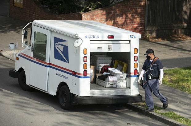 A mail carrier wearing a mask and gloves in Berkeley on March 27, 2020. Postal employees are considered essential during the shelter in place. - PHOTO BY ANNE WERNIKOFF FOR CALMATTERS